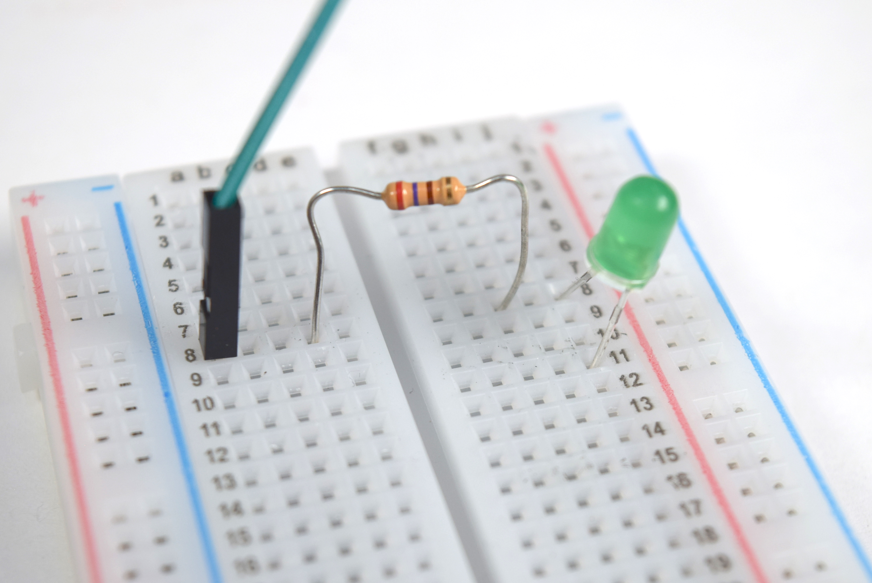 Photograph of a resistor's short leg connecting to an LED's long leg in the same row.