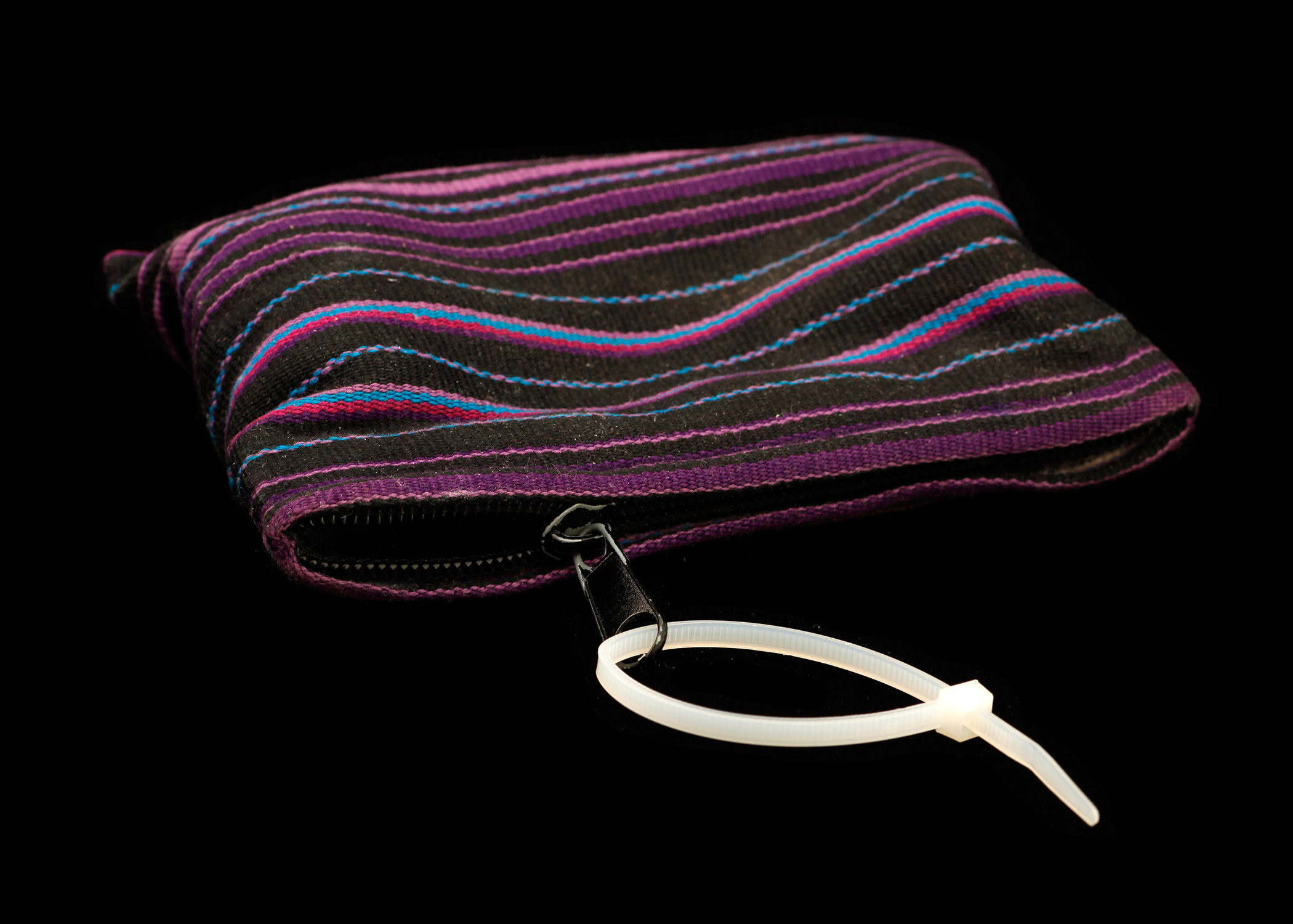 Image of small fabric pouch with zipper closure. The zipper has a white cable tie loosely affixed through it so that it forms a loop of perhaps 2" diameter.