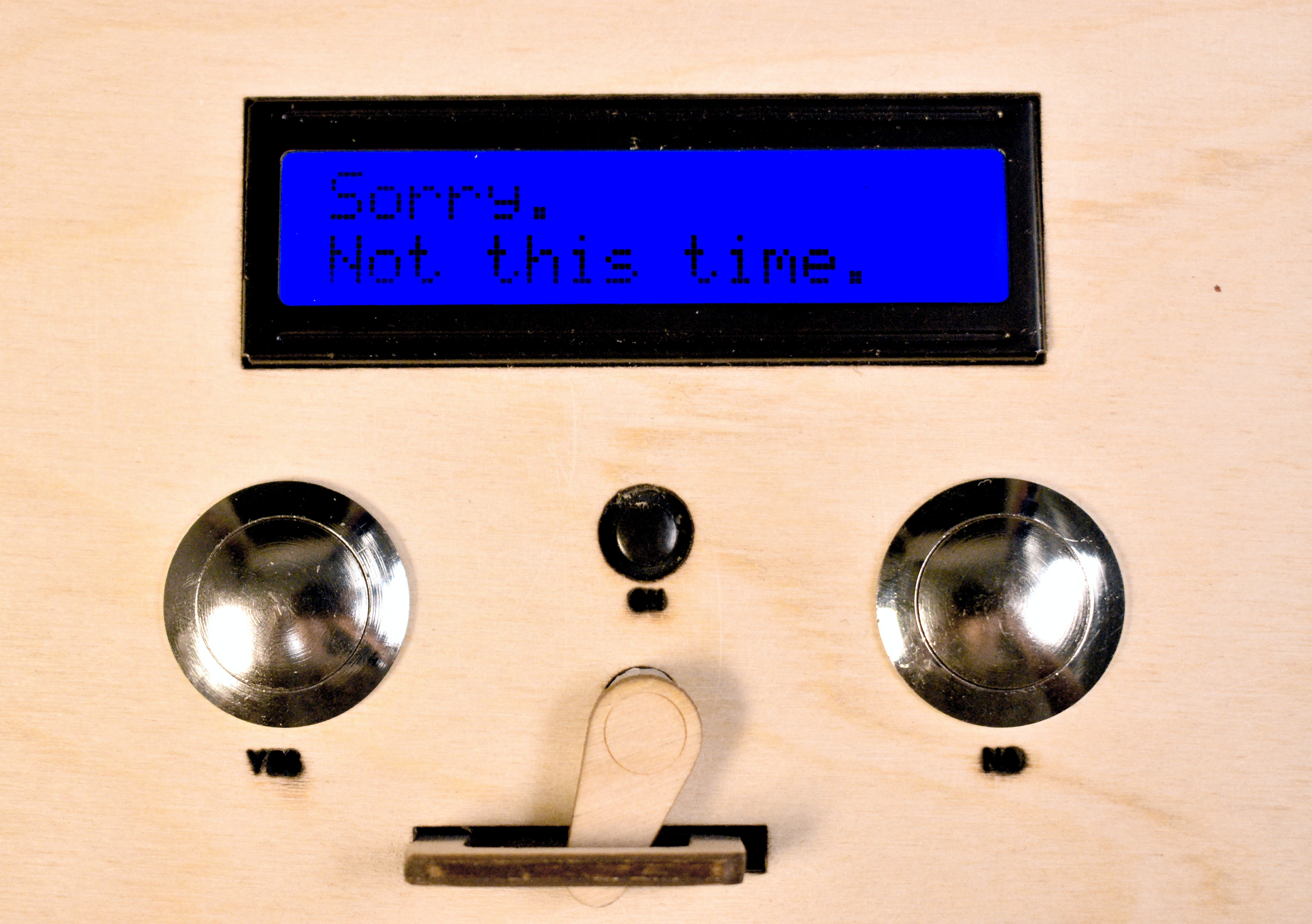 Closeup image of a digital display reading "Sorry. Not this time." Beneath it are two metal buttons labeled "yes" and "no," and a wooden latching mechanism.