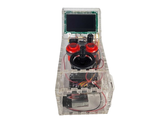 Clear plastic box with colored buttons and a joystick on the top of it, and a small black screen facing the camera that projects out of the base of the box. Inside the box, electronics and a 9 volt battery are visible.