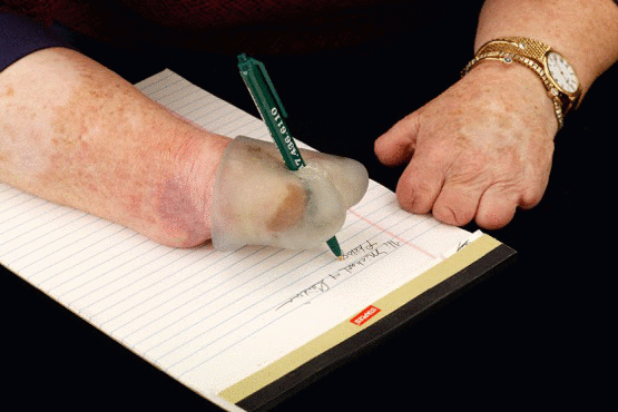 Looping movie of an end-of-arm prosthetic, made of clear plastic, on the end of Cindy's right arm. With the prosthetic holding the pen, she is writing on a legal pad.