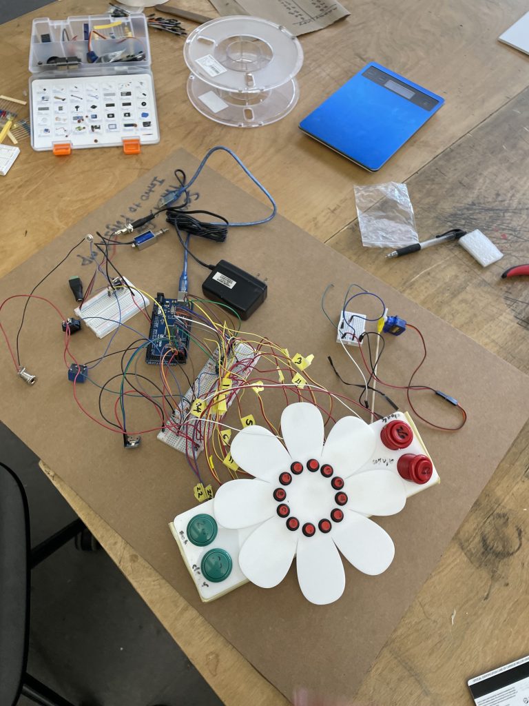 On top of a table sits a big piece of cardboard. On top of the cardboard are wires connecting buttons and switches to the clock interfcae we prototyped with white acrylic