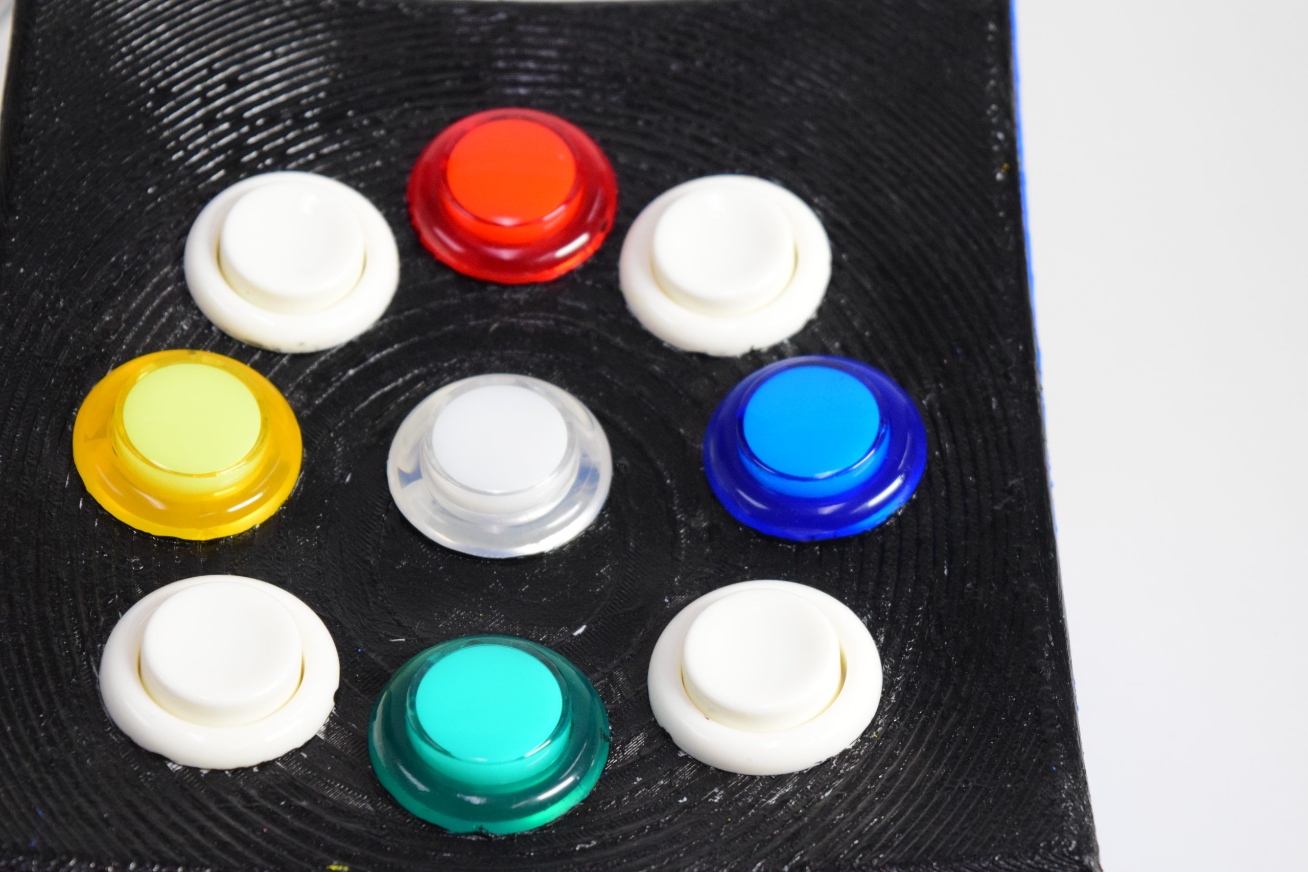 A curved black surface with 9 arcade buttons. 8 of the arcade buttons are arranged in a circle and the 9th button lies in the center.