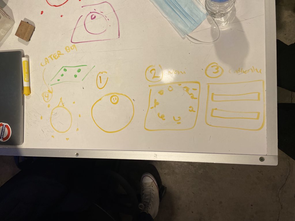 Drawn on a whiteball table with yellow marker are sketches of different clock interfaces