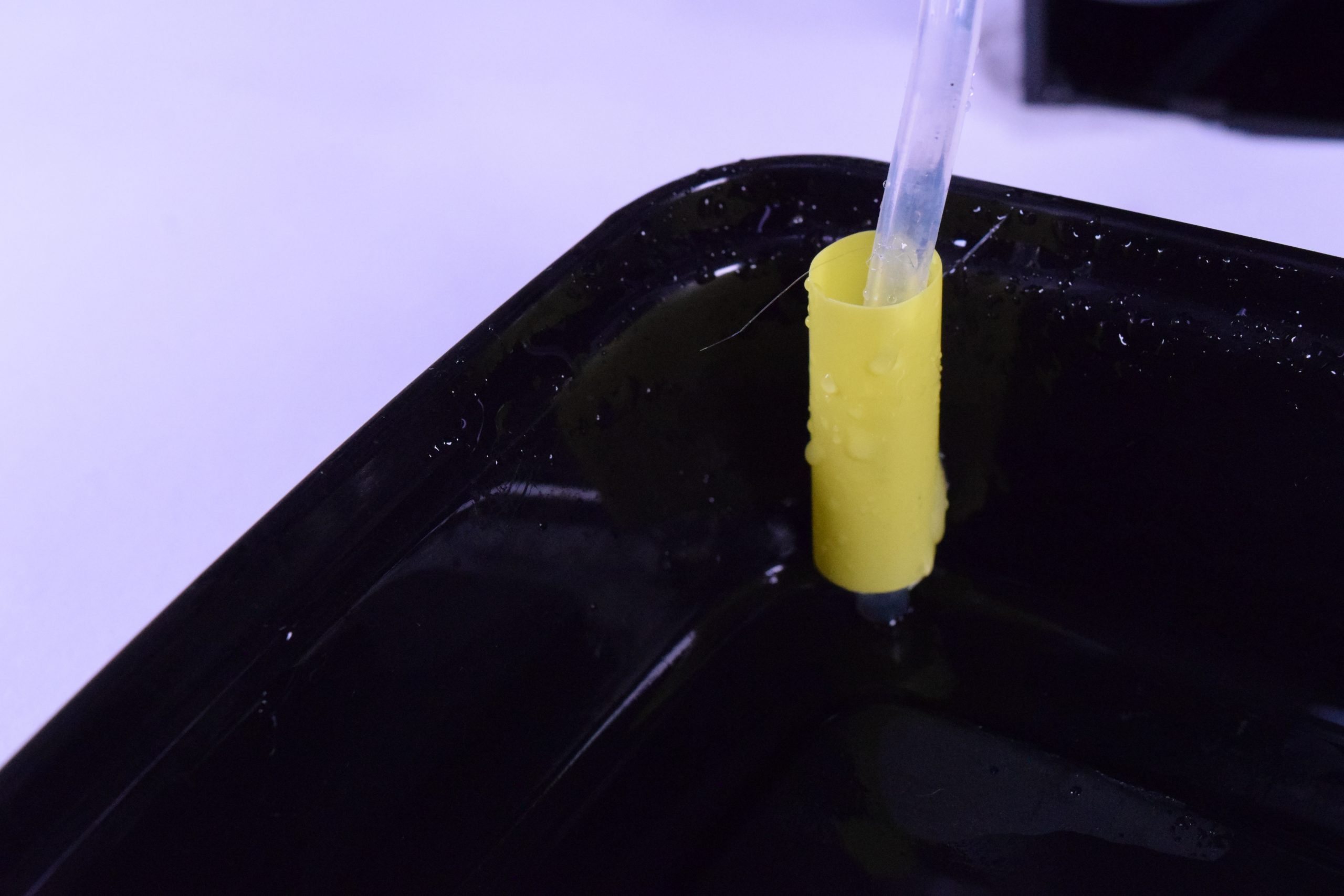 Close-up of a piece of a yellow drinking straw to help guide the tube responsible for bringing water up to the top water container.
