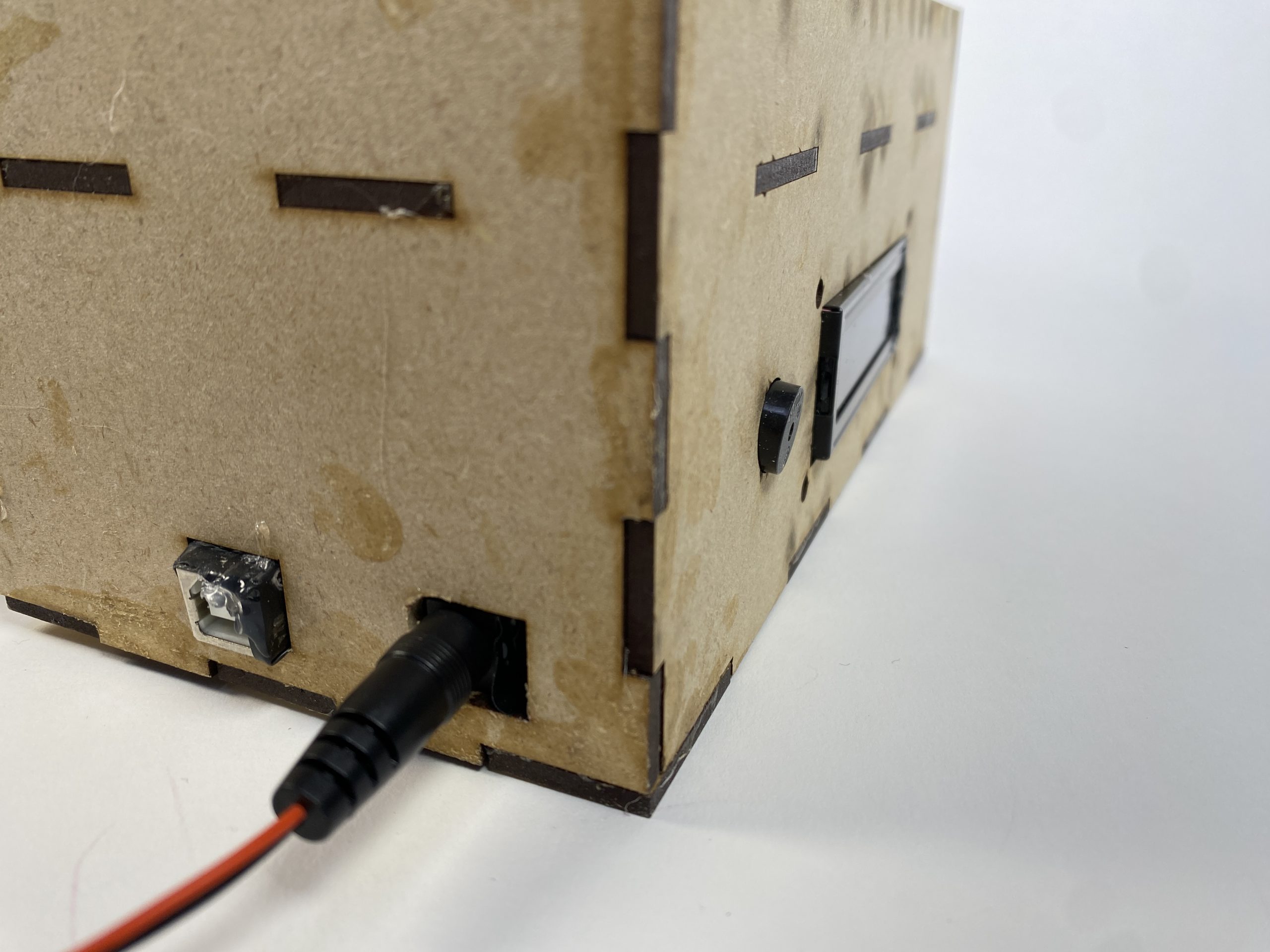 The back-facing view of a wooden box. There are two holes cutout, with a DC jack sticking out & connected to some wires.