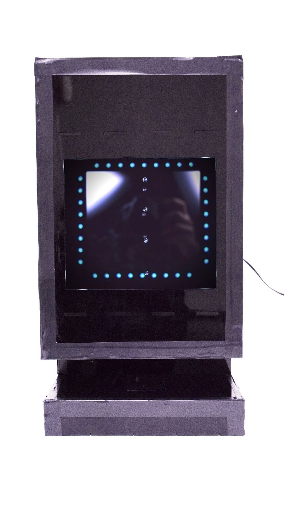 Front view of the Droplet Distracter, a black box with a large slot for a phone and a viewing window. There is an LED strip outlining the internal of the viewing box and there are 4 droplets suspended in mid air in the viewing box.