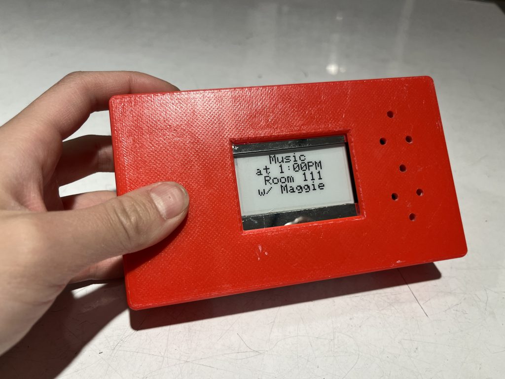 Hand holding red box with white screen in the middle and 7 holes to the side