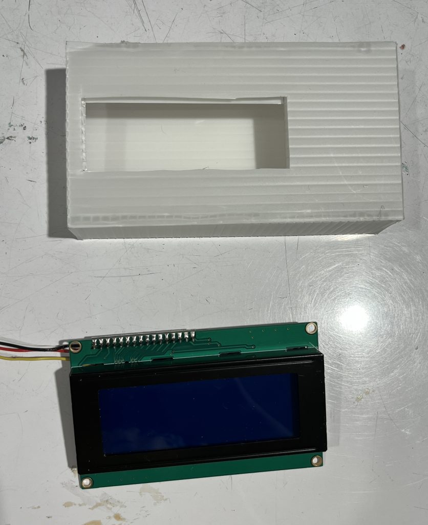White box with hole cut into it and an LCD display module laid out on a table