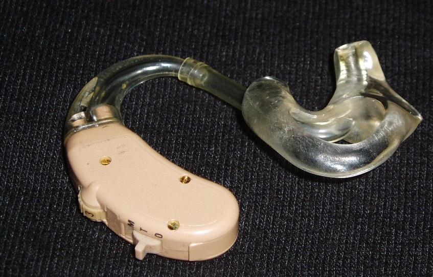 Traditional hearing aid: a pink flesh-tone bean-shaped electronic device is paired with a clear plastic tube which ends in a molded clear piece to fit into the ear canal.