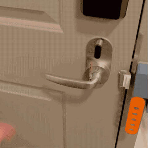 Gif showing a person trying to open the door to their apartment, but when the handle is pushed, an orange plastic arm pivots up to block the door. Then, they swipe a key fob at the machine, and the next time they try the handle, the door opens without being blocked.