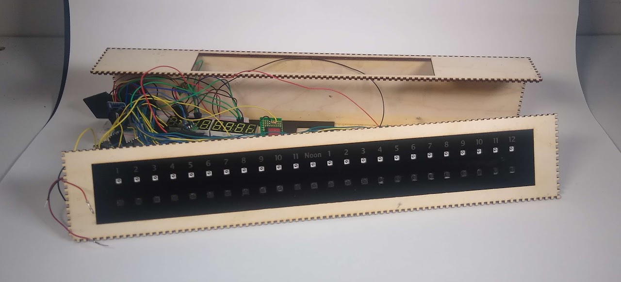 Long, narrow wooden box with black plastic inset labeled at the left 1 through 11 and then noon in the center, then 1 through 12 on the right. The box is partly disassembled and wires and other electronic internals are visible through the opening.